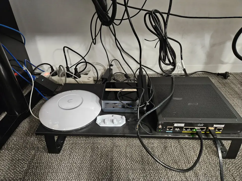 A router, mini PC and Wi-Fi access point on a stand under a desk