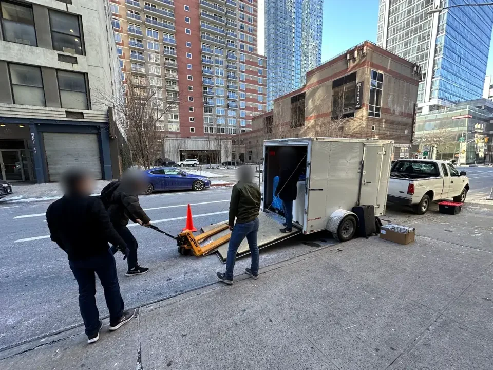 A crew loading a cargo trailer with a pallet jack at the kerb