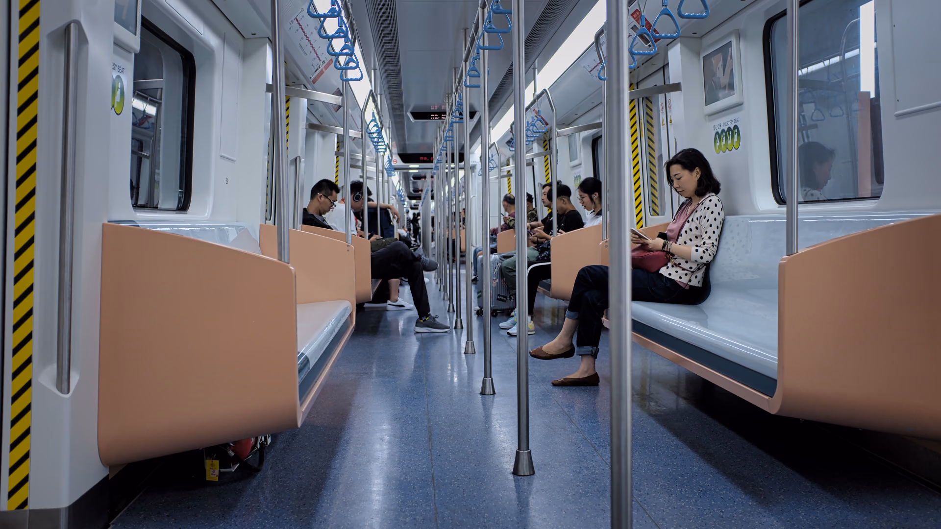 Passengers seated in a train carriage, with seats, floor and grab rails visible along its length